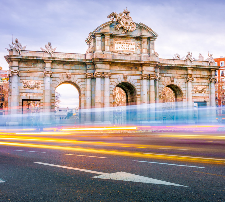 A shot of The Alcala Door (Puerta de Alcala), a post-Roman triumphal arch with cars passing by and buildings in the background in Madrid, Spain. 