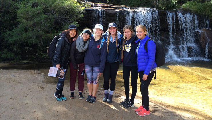 Six students smiling near a waterfall in Sydney, Australia.