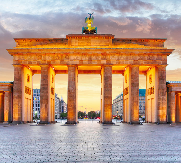 Brandenburg Gate lit up with an orange glow at dusk in Berlin, Germany.