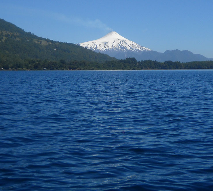 The snow covered Volcán Villarrica behind a big blue lake in Villarrica, Chile.