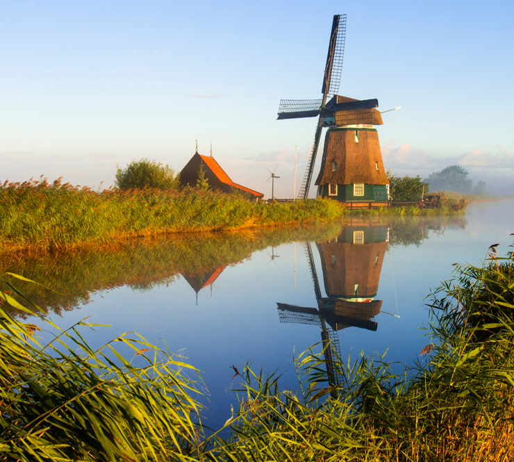 Landscape shot of windmill near a body of water and row crops in Wageningen, Netherlands. 