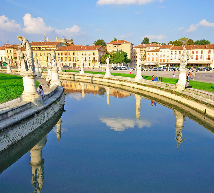 The elliptical square of Prato della Valle with a large space with a green island at the center and surrounded by a small canal bordered by two rings of statues in Padova, Italy. 