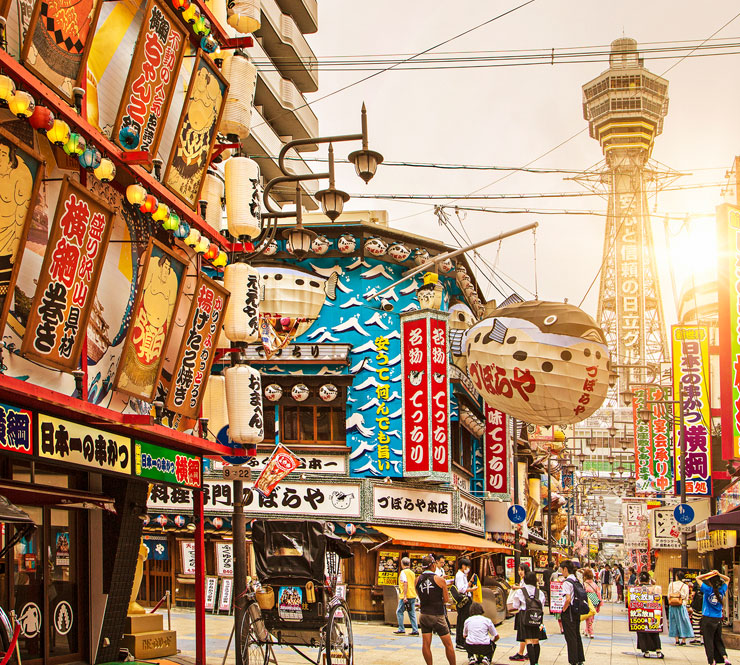 The colorful Shinsekai District glows in the bright sunshine with Tsutenkaku Tower in the background in Shinsekai, Osaka, Japan. 