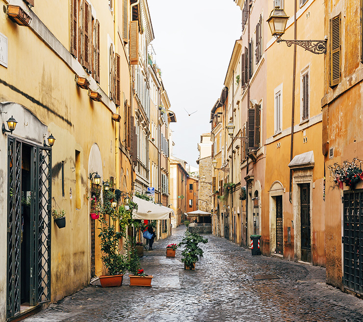 Golden walls, color-filled flower pots, and cobblestones line a street in the Trastevere neighborhood in Rome.