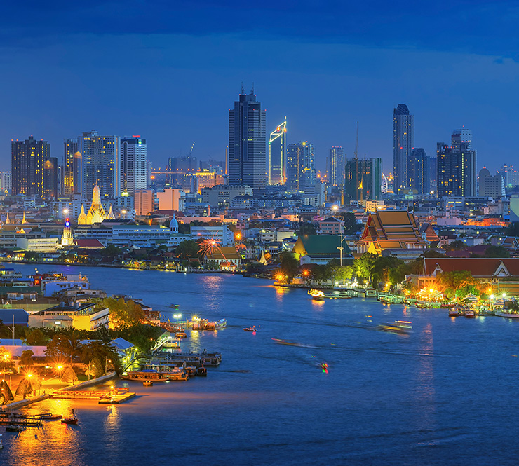 The Chao Phraya River Wat Arun curves around high-rise buildings at dusk in Bangkok, Thailand..