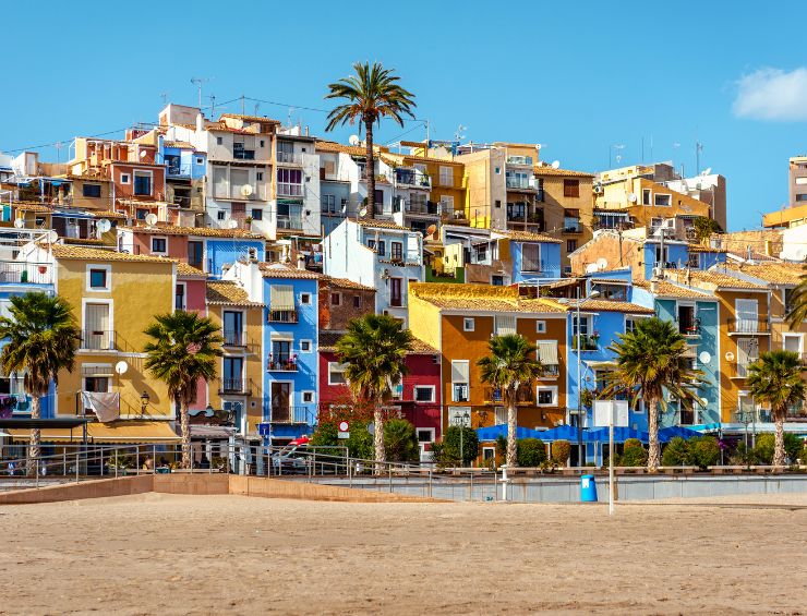 A street lined with palm trees and multicolored townhouses on the beach.