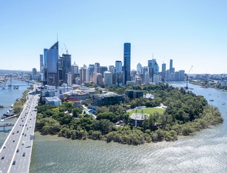 Aerial view of the Brisbane CBD from over the Brisbane River on a cloudless blue sky day with a busy bridge in the foreground and the Queensland university Garden’s Point campus in the cbd foreground