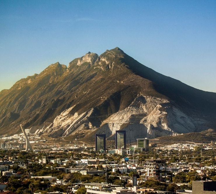 Sunlight rising over a large mountain, the skyline of Monterrey in the foreground.
