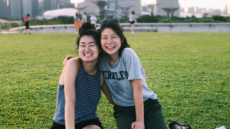 Kristen Wehara from UC Berkeley and friend smiling on a grass lawn at Marina Barrage in Singapore.