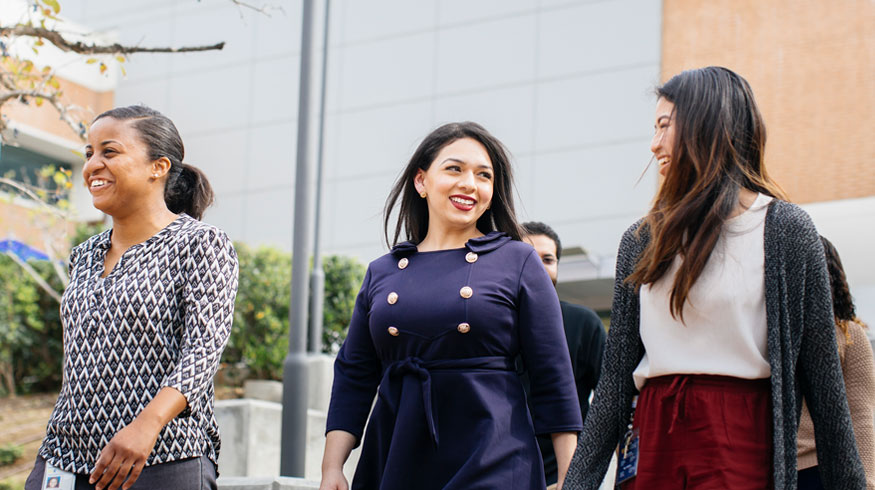 Three female students walk on campus with smiles on their faces.