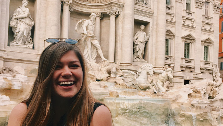 UCSB student Rachel smiles big in front of the famous Trevi Fountain with its aqua water and statues.