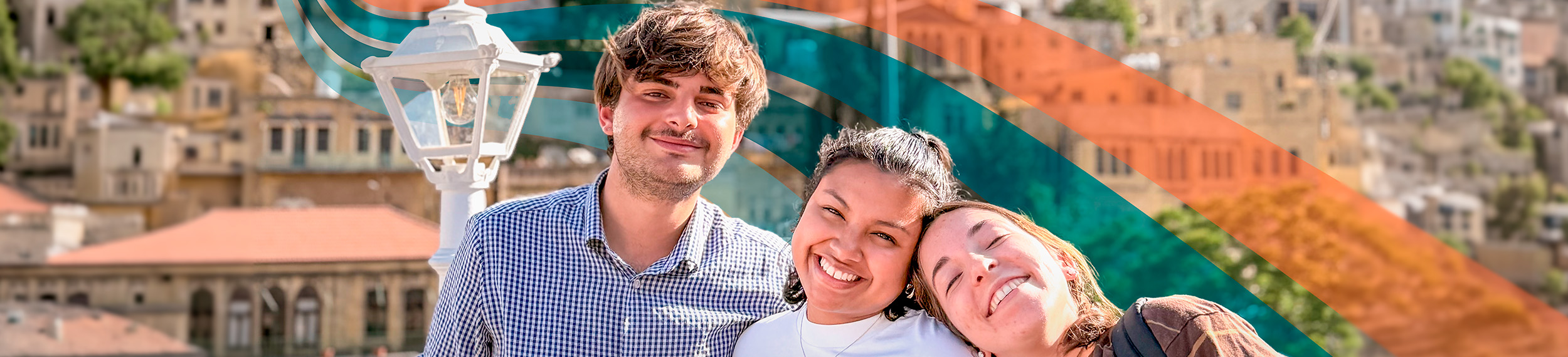 Three friends smiling with buildings covering hillside in background, Jordan.