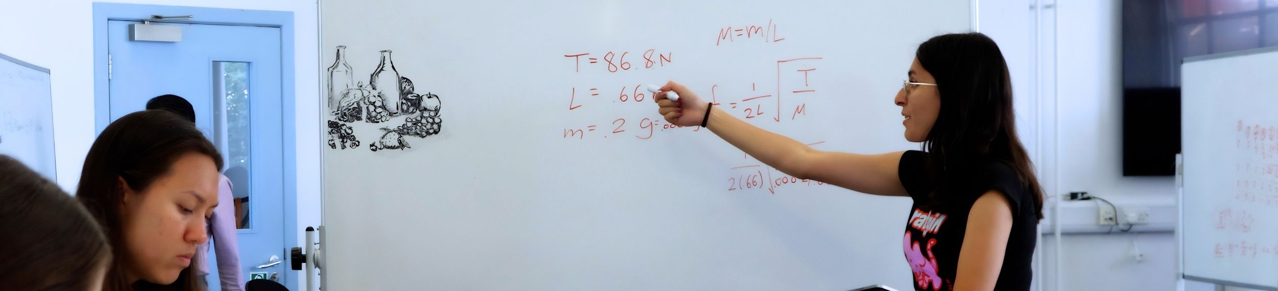 A student writes out equations on a whiteboard in front of other students in a classroom. 