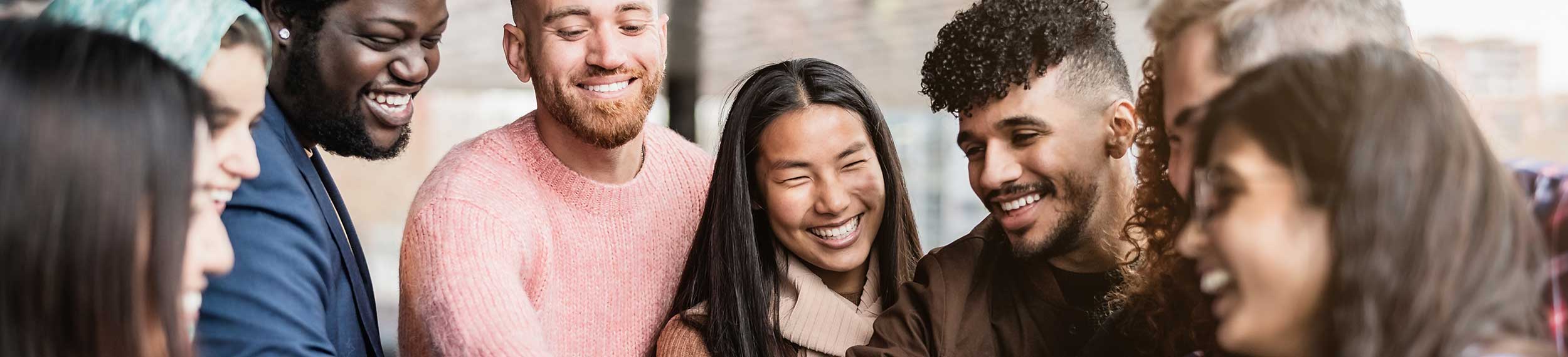 A groups of diverse young friends stacking hands together outdoors.