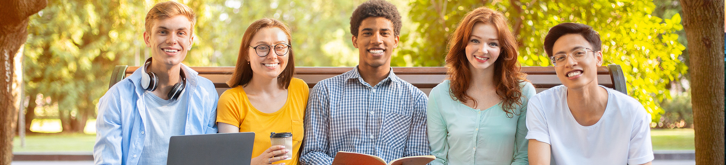 Five students smiling and laughing on a bench. 