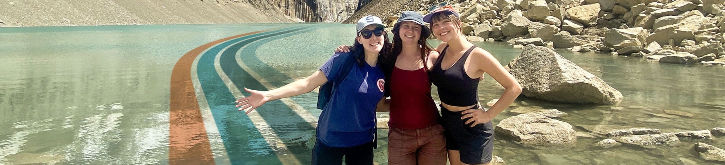 Group of friends standing on shoreline rocks in a mountain lake.
