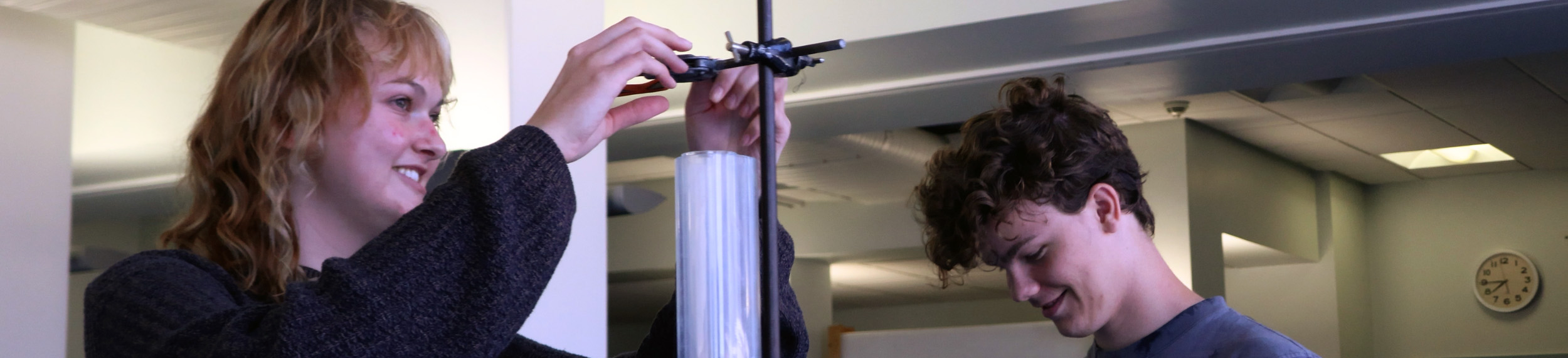 Two students smile while conducting measurement using a tube, in a classroom in Glasgow, Scotland.