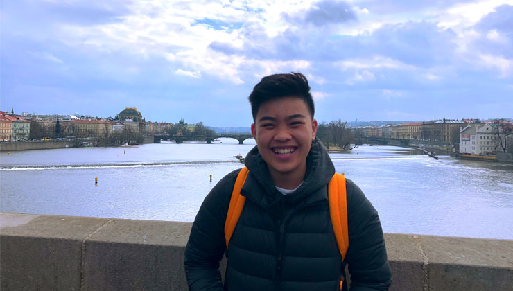 Student smiling near the river and a view of Prague, Czech Republic.