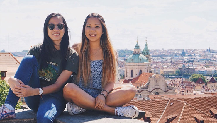 Two friends smiling on the rooftops and a view of Prague, Czech Republic in the background.