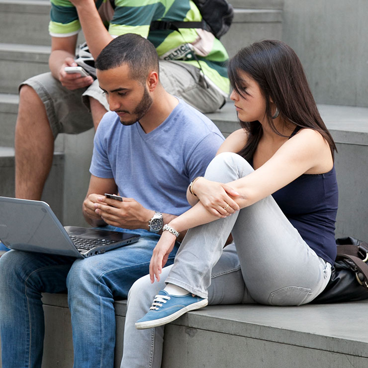 Two student look at a computer screen while sitting on steps.