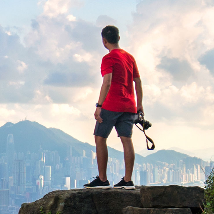 Man with camera looks at Hong Kong from on top of a hill on a cloudy day.