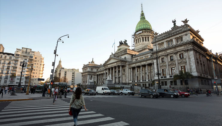 A woman walks across the street with he Argentine National Congress in the background in downtown Buenos Aires, Argentina.
