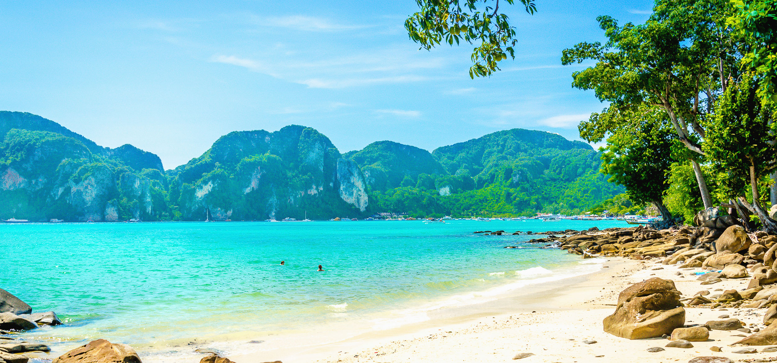 Verdant mountains make for a beautiful background to clear blue waters of a beach in Thailand.