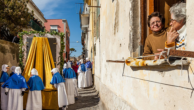 Two adults looking out the window to watch a Good Friday Procession in Procida Italy.