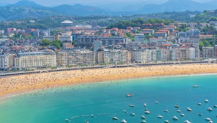 Large Apartment complexes line a sandy beach, bright blue water washes against it.