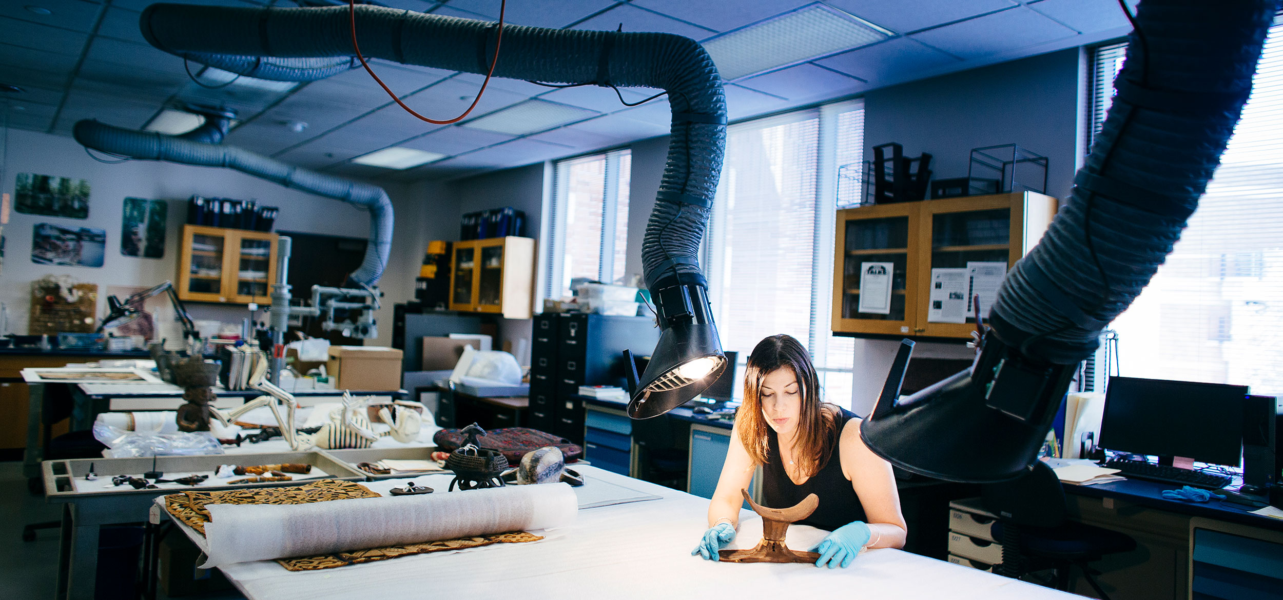 Student examining a single artifact with the rest of the collection in a classroom. 