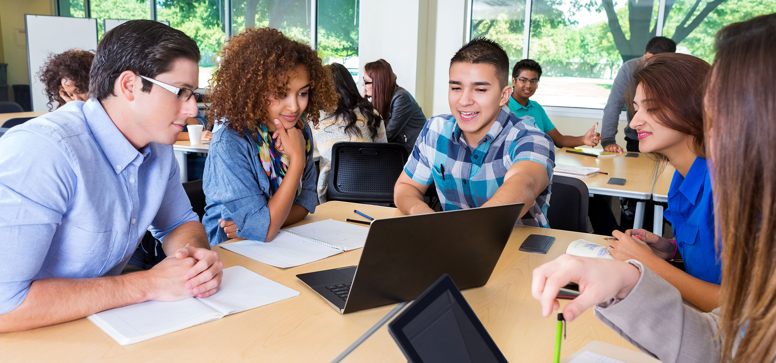 Five students sitting at a table and learning around a laptop. 