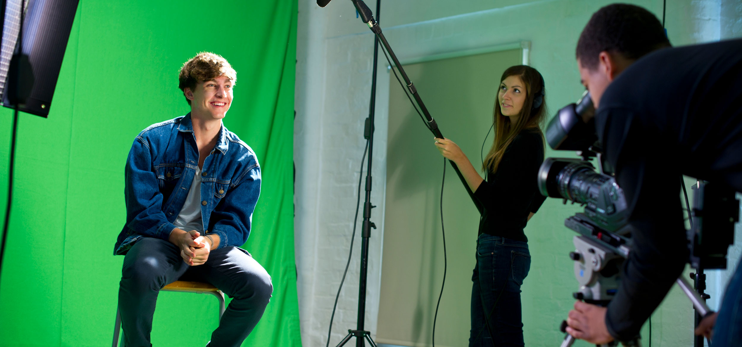 A media student being interviewed against a green screen in a college tv studio.