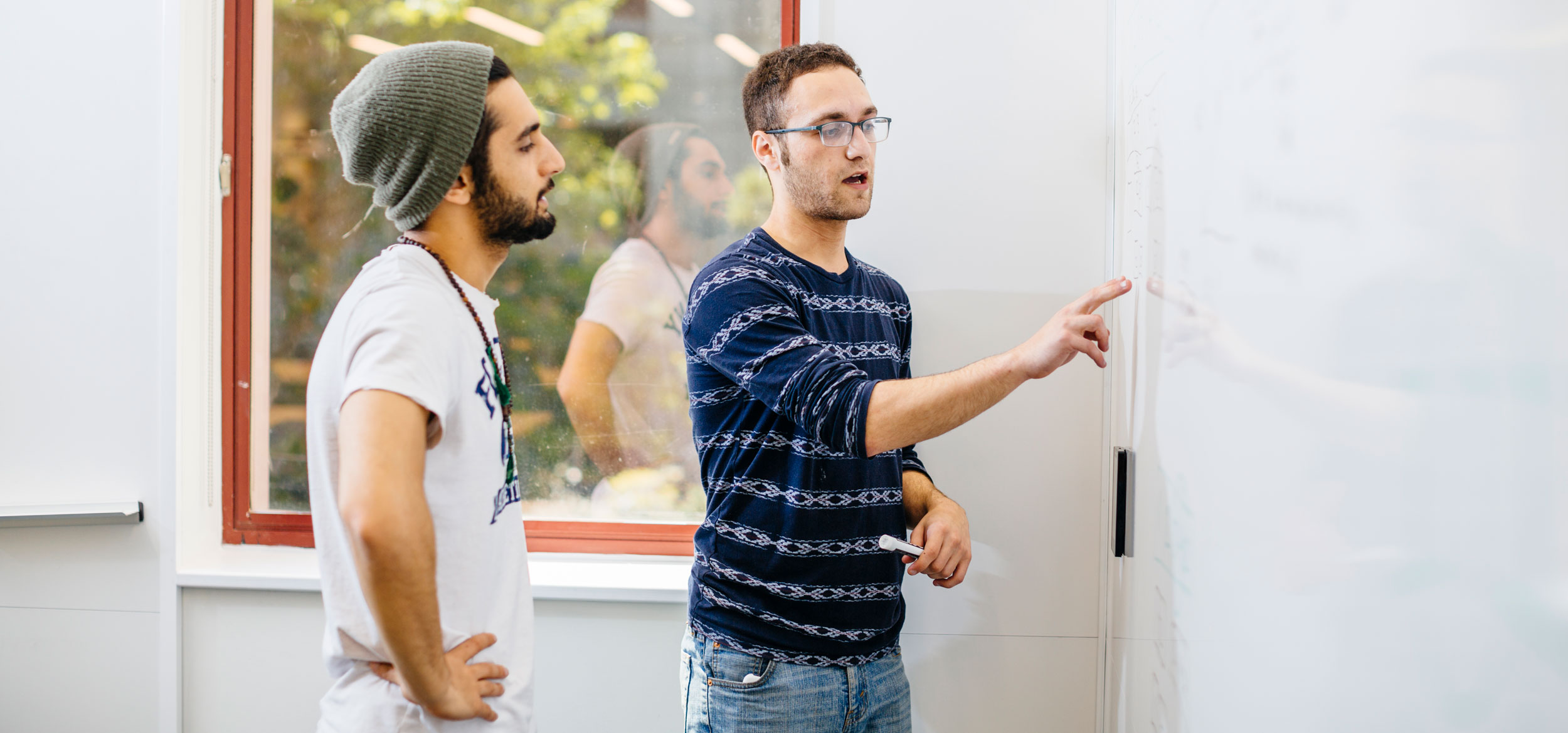 Two students go over a linguistics concept while standing and working on a white board. 