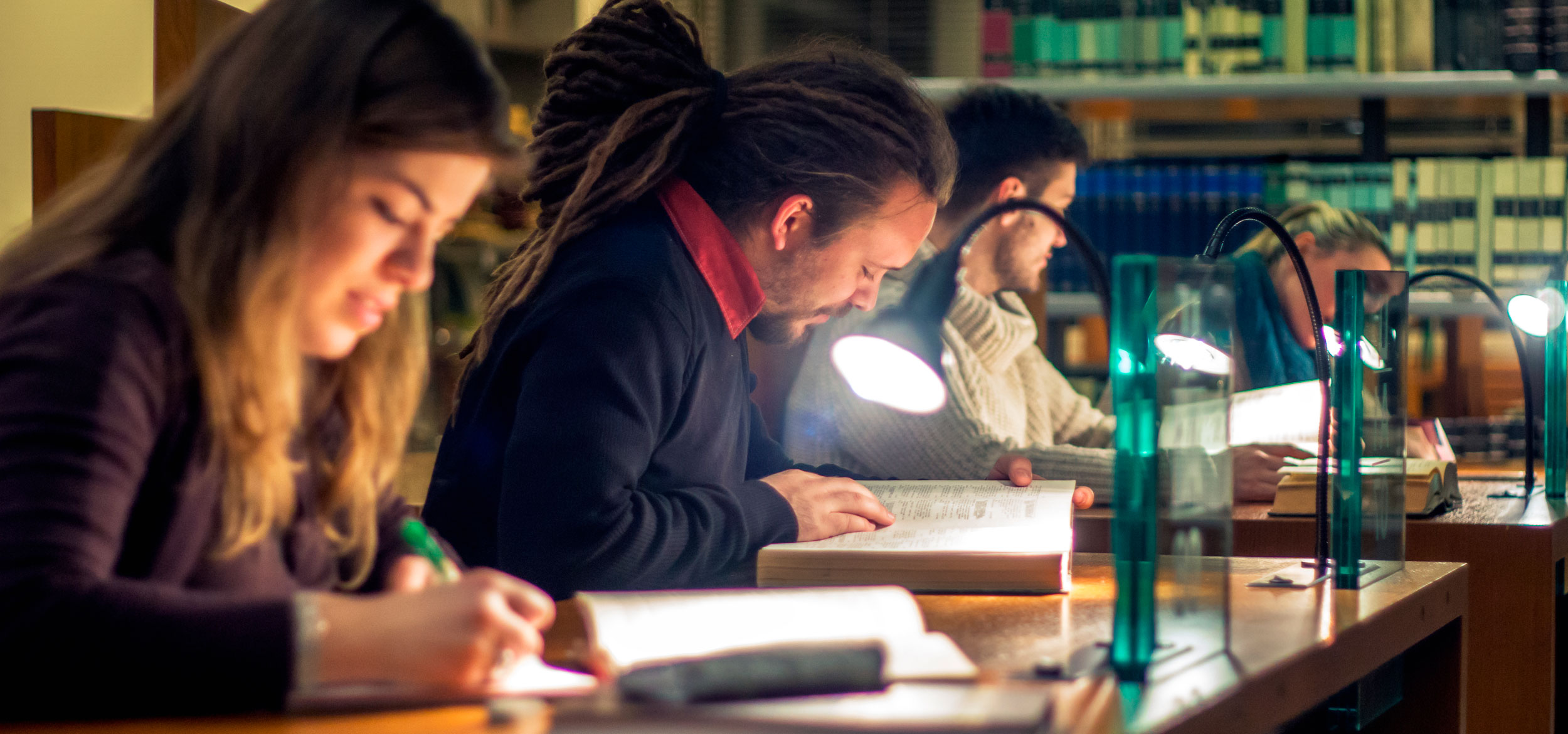 Three students study at desks in a library. 