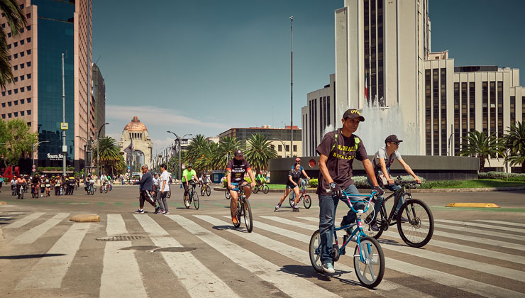 Bicyclists ride across an intersection on a sunny day in the Business District of Mexico City, Mexico.