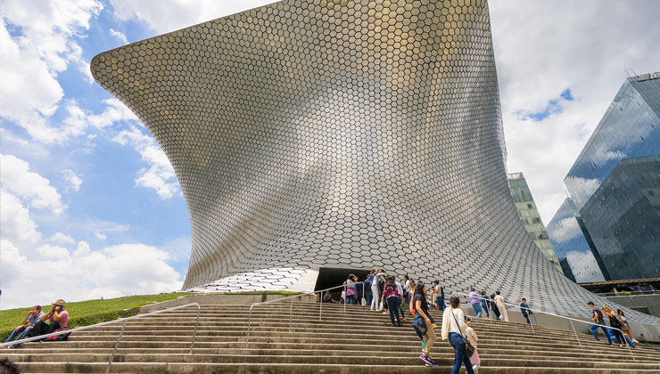 Tourists walk up the steps of Soumaya Museum, which looks like a giant piece of curved metal. It is located in Nuevo Polanco in Mexico City, Mexico.
