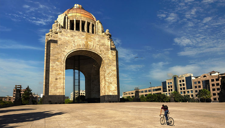 A cyclist rides on the square in front of the Monument of the Revolution, which glows brightly in the sun, in Mexico City, Mexico.