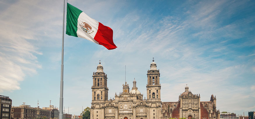 The Mexican flag blows in center of Zocao Square with a view of the Mexico City Cathedral and President's Palace in Mexico City, Mexico.