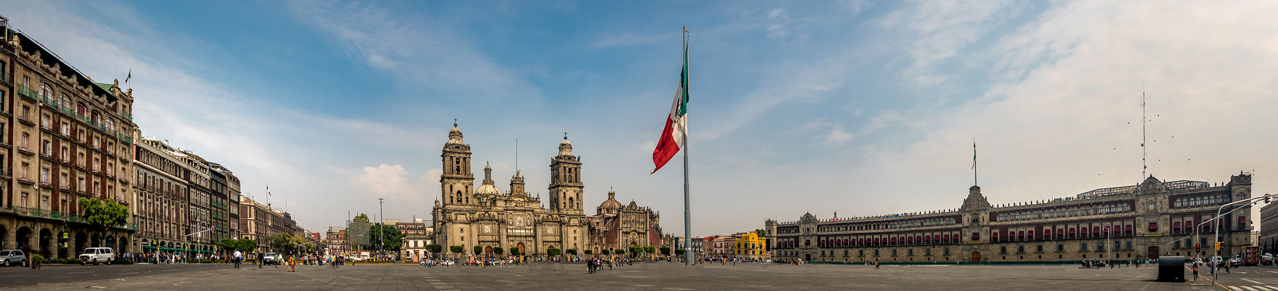 The Mexican flag blows in center of Zocao Square with a view of the Mexico City Cathedral and President's Palace in Mexico City, Mexico.