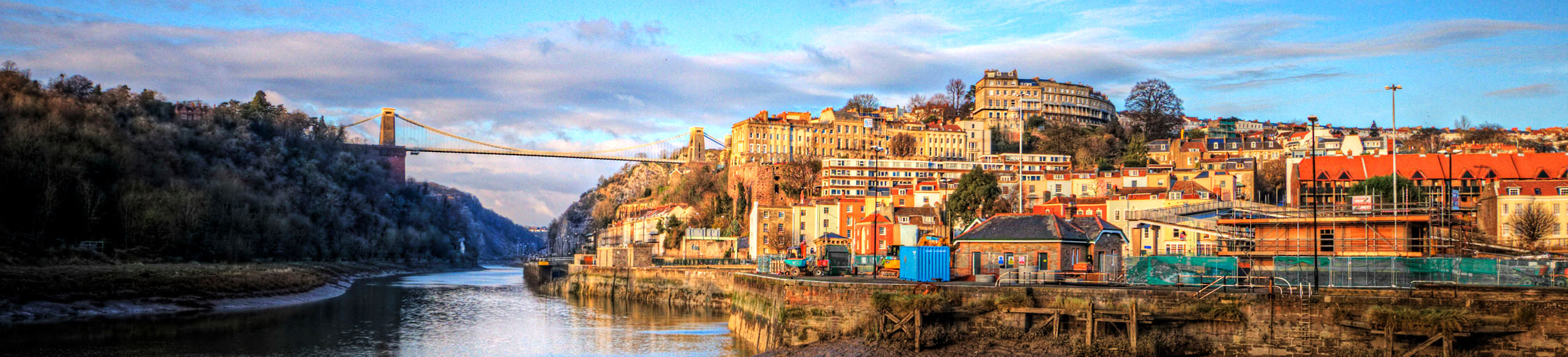 View from riverbank of Clifton Suspension Bridge and waterfront buildings, Bristol