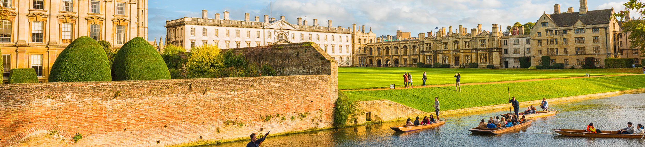 In front view boats on the river with tourists, in background Kings College, green grass and blue sunny sky.