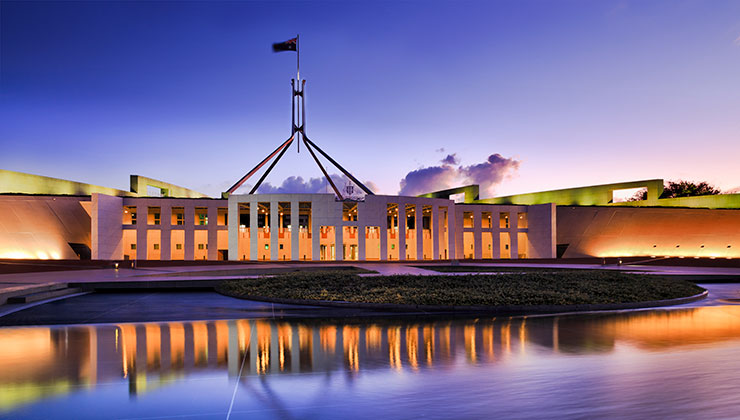View of Parliament House at sunset with a reflection in the water.