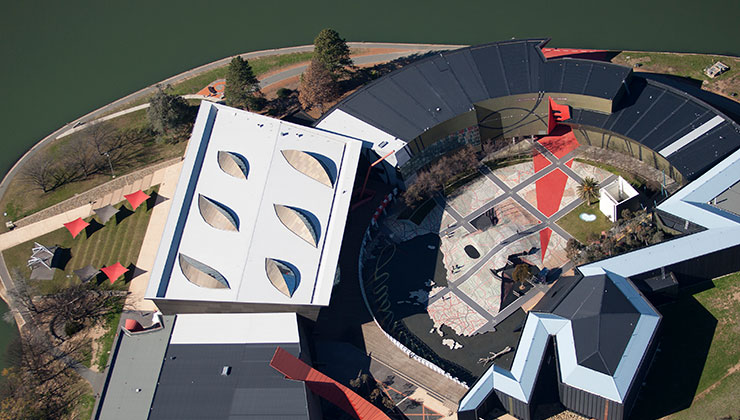 Aerial view of museum around a lake, few people walking around enjoying the sunny day.