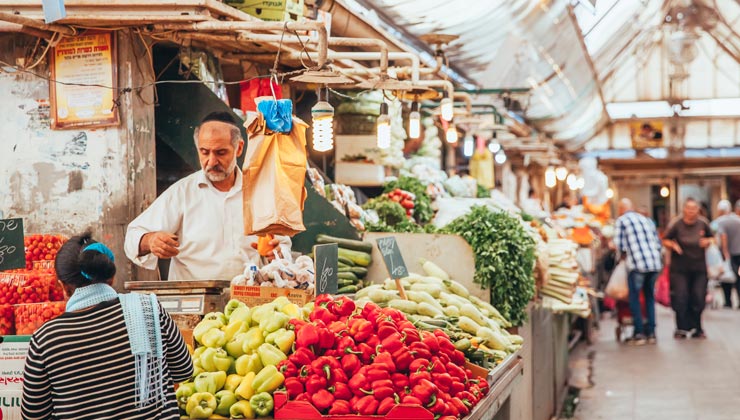 Market vendor talking to customer with colorful produce at Mahane Yehuda Market in Jerusalem, Israel.