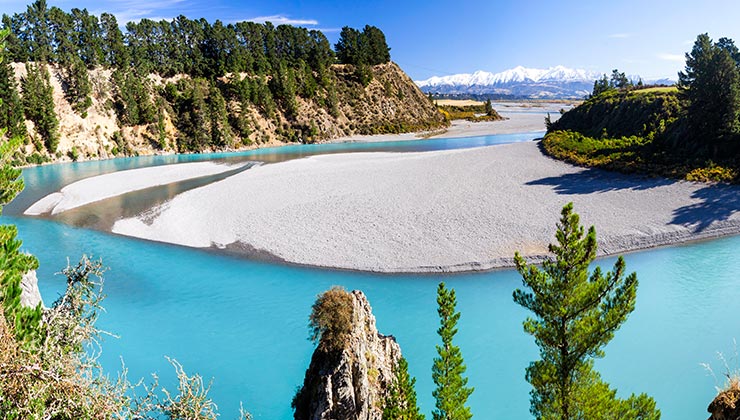 Blue waters of Waimakariri River funnel through the Waimak Gorge with the snow capped Southern Alps in the distance.