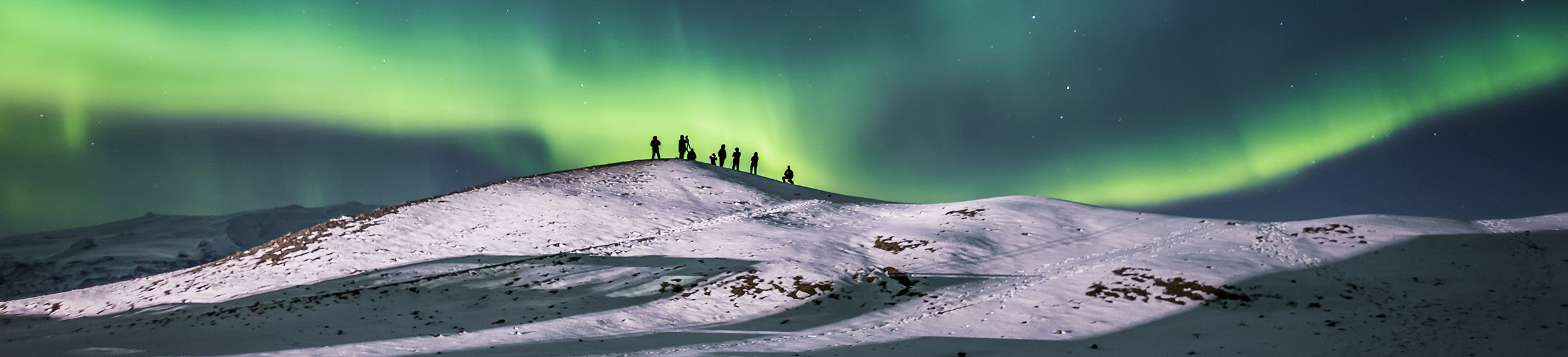 People walk in the snow under the Northen Lights in Iceland. 