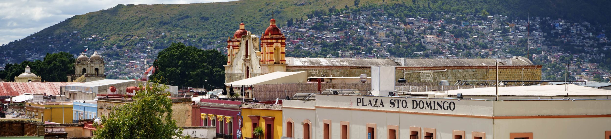 High angle of a colorful plaza square of buildings and a large crowd, with rolling hills in the background.