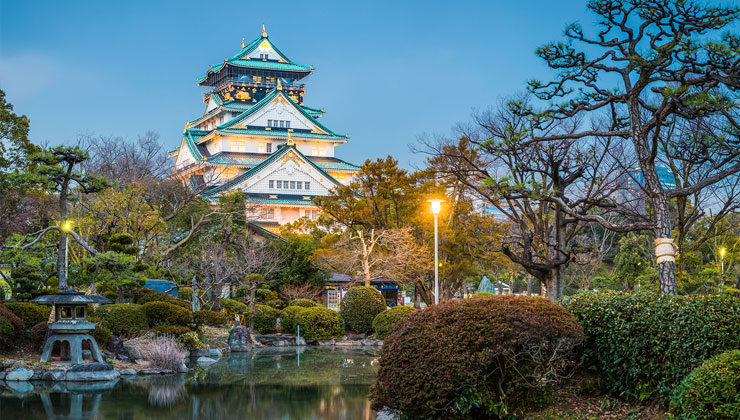 Osaka Castle illuminated at dusk reflecting in tranquil pond Japan.