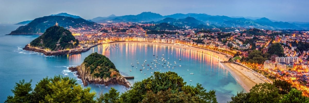 Panoramic view from above of a bay lit by city lights, with boats floating in the water