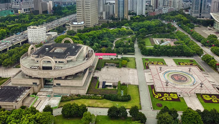 Open square with gardens and trees around a circular building in Shanghai, China. 